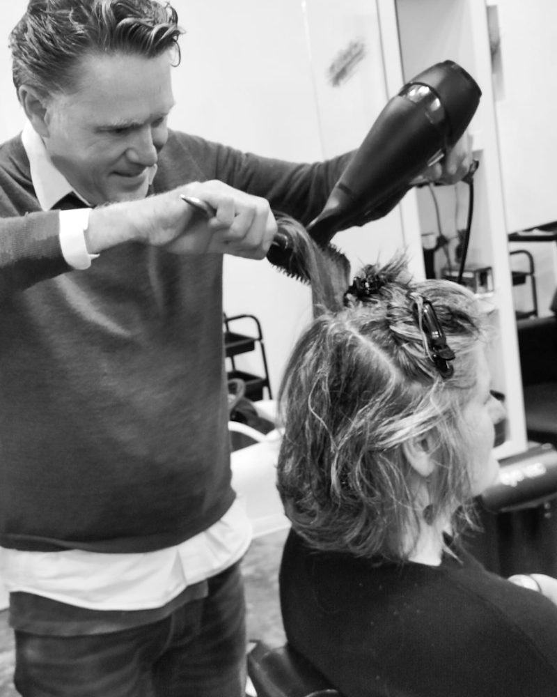 a male hair stylist blowdrying a customer's hair